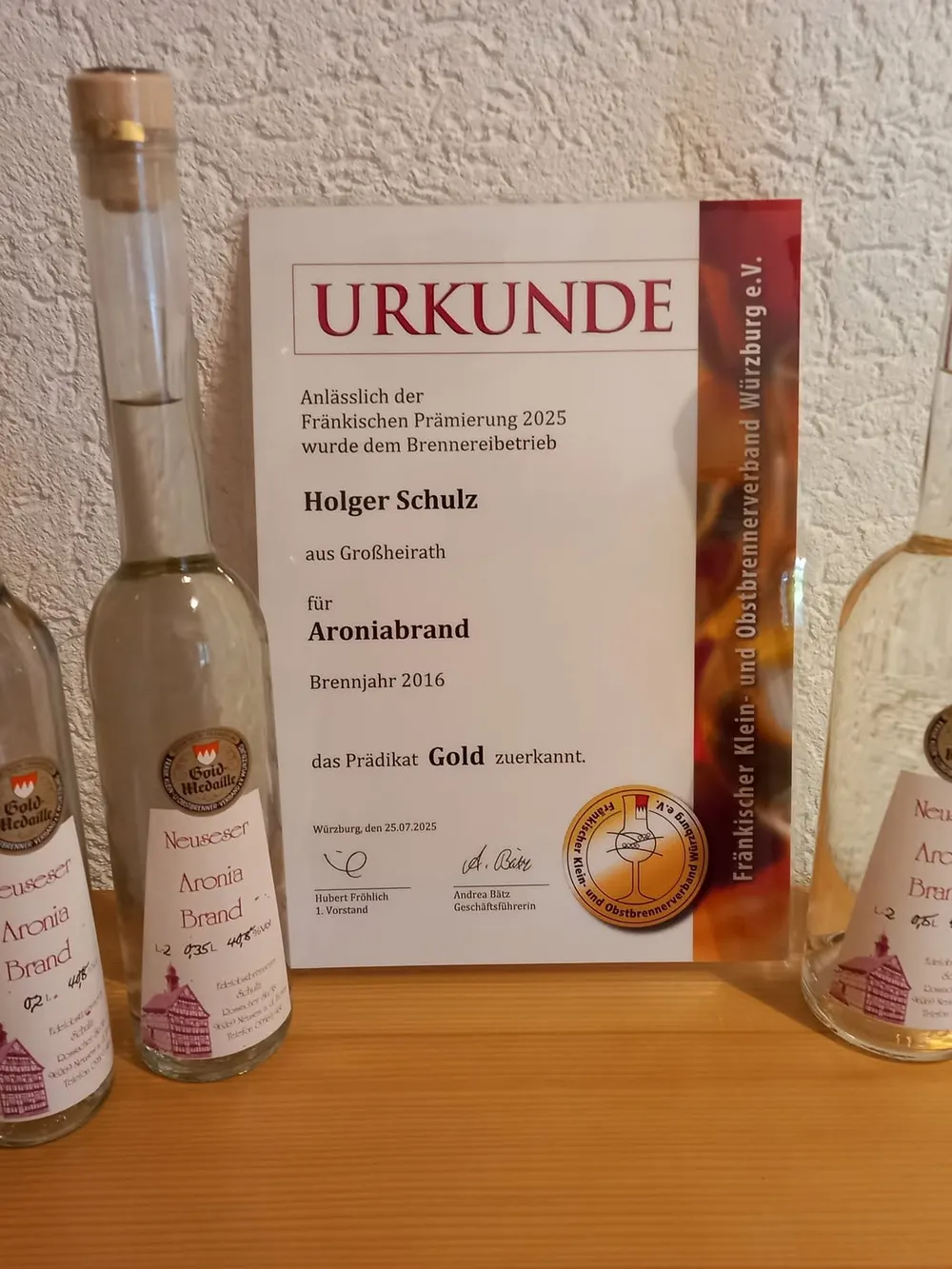 Goldurkunde für den Aroniabrand, davor drei Flaschen der Brennerei