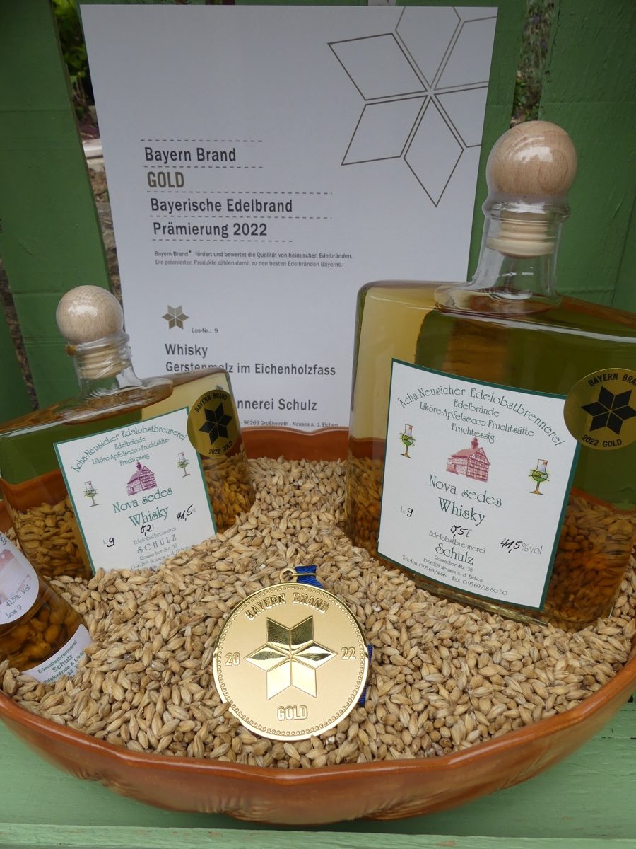 Zwei Flaschen Nova sedes Whisky mit Goldmedaille in einer Schale Gerste